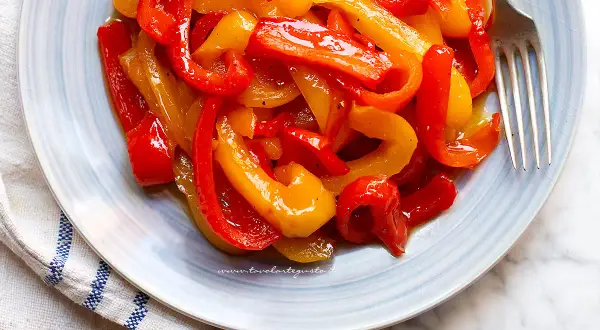 Peperoni in agrodolce, un contorno colorato e saporito, servito su un piatto azzurro con forchetta.