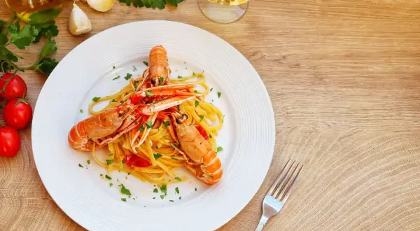 Un piatto di linguine con scampi, pomodorini e prezzemolo, uno dei migliori primi di pesce, pronto per essere gustato con un bicchiere di vino bianco.