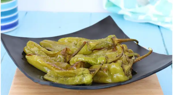 Friggitelli al forno, verdi e lucidi, serviti su un piatto nero. Un contorno saporito e facile da preparare.