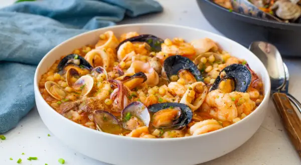 Un invitante piatto di fregola sarda con frutti di mare freschi: cozze, vongole, gamberi e calamari, condito con erbe aromatiche.