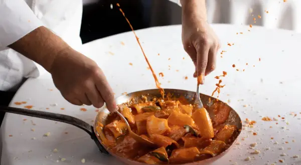 Chef mescola paccheri alla Vittorio, la salsa rossa schizza in un'esplosione di sapore.