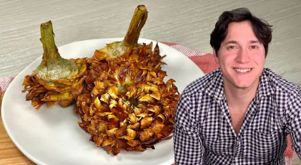 Due carciofi alla giudia dorati e croccanti su un piatto bianco, accanto a un uomo sorridente.