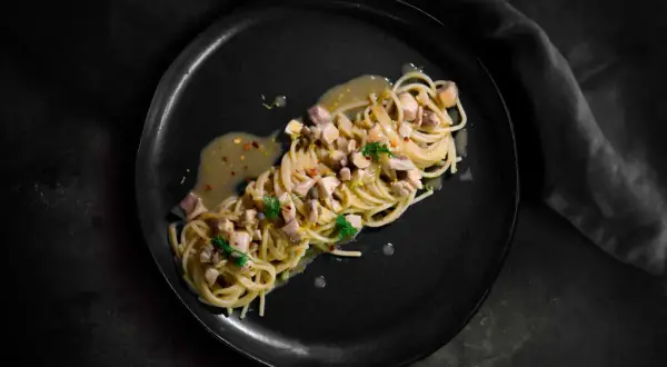 Spaghetti con ricciola, limone e peperoncino su piatto nero. Un piatto elegante e saporito.
