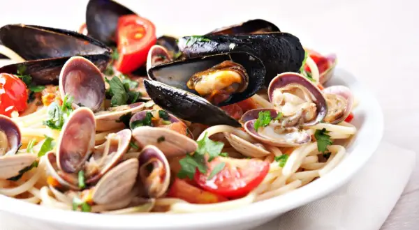 Un piatto invitante di tagliolini ai frutti di mare, con cozze, vongole e pomodorini freschi, guarnito con prezzemolo.