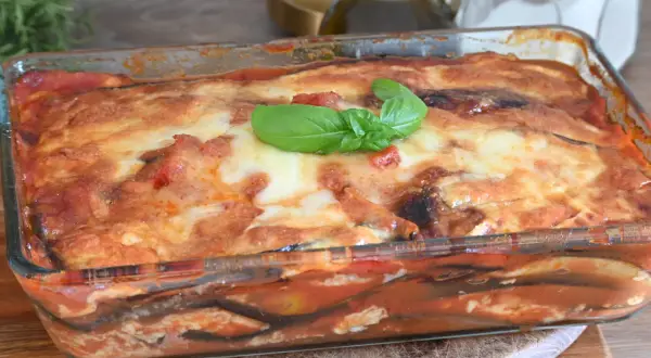 Parmigiana di melanzane non fritte, appena sfornata in teglia di vetro, con basilico fresco.