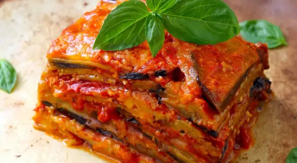 Una fetta di parmigiana di melanzane ricetta originale, stratificata e succulenta, guarnita con basilico fresco.