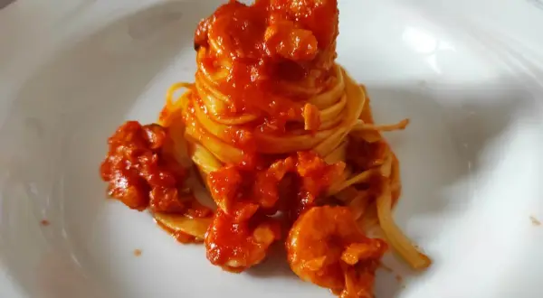 Un nido di pasta fresca avvolto in un ricco sugo di pesce, con gamberi succulenti che si adagiano sul piatto bianco.