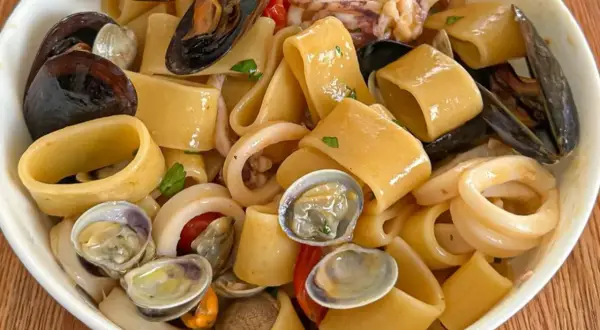 Un piatto invitante di calamarata allo scoglio, con pasta grossa, cozze, vongole e anelli di calamaro, condito con pomodorini e prezzemolo.