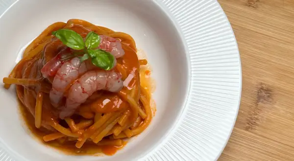 Spaghetti conditi con un sugo rosso intenso, guarniti con gamberi rosa e basilico fresco. Un piatto che evoca il sapore del mare, come una ricca bisque di crostacei.