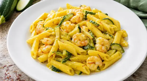 Piatto di pasta penne con zucchine e gamberetti, condito con una salsa cremosa e fili di zafferano.