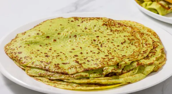 Piatto di crepes di zucchine verdi, sottili e leggermente dorate, impilate su un piatto bianco.
