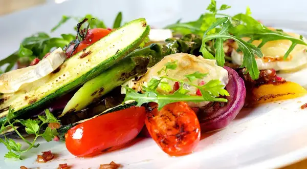 Deliziosi contorni estivi: zucchine grigliate, pomodorini, cipolla rossa e formaggio di capra su un letto di rucola.