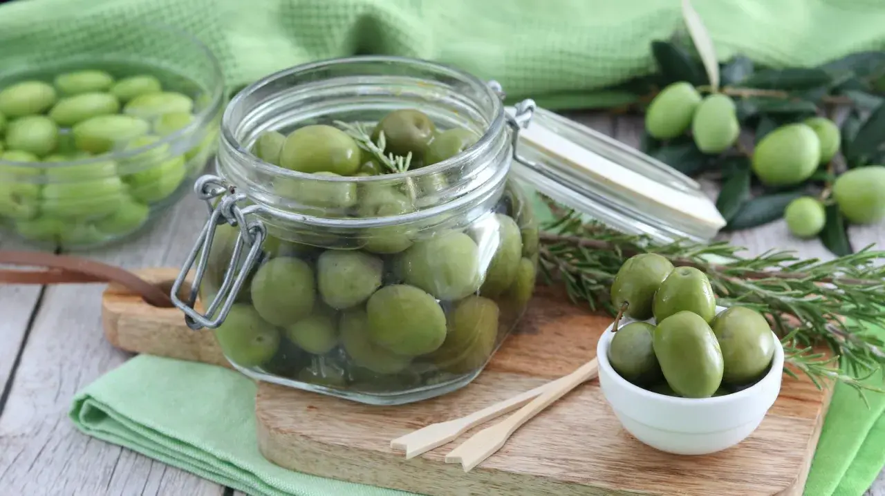 Verdi olive in salamoia per olive, conservate in un barattolo di vetro con rametti di rosmarino.