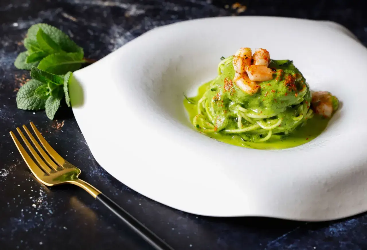 Spaghetti di zucchine con gamberi e salsa verde, guarniti con paprika e menta fresca. Un piatto leggero e colorato.