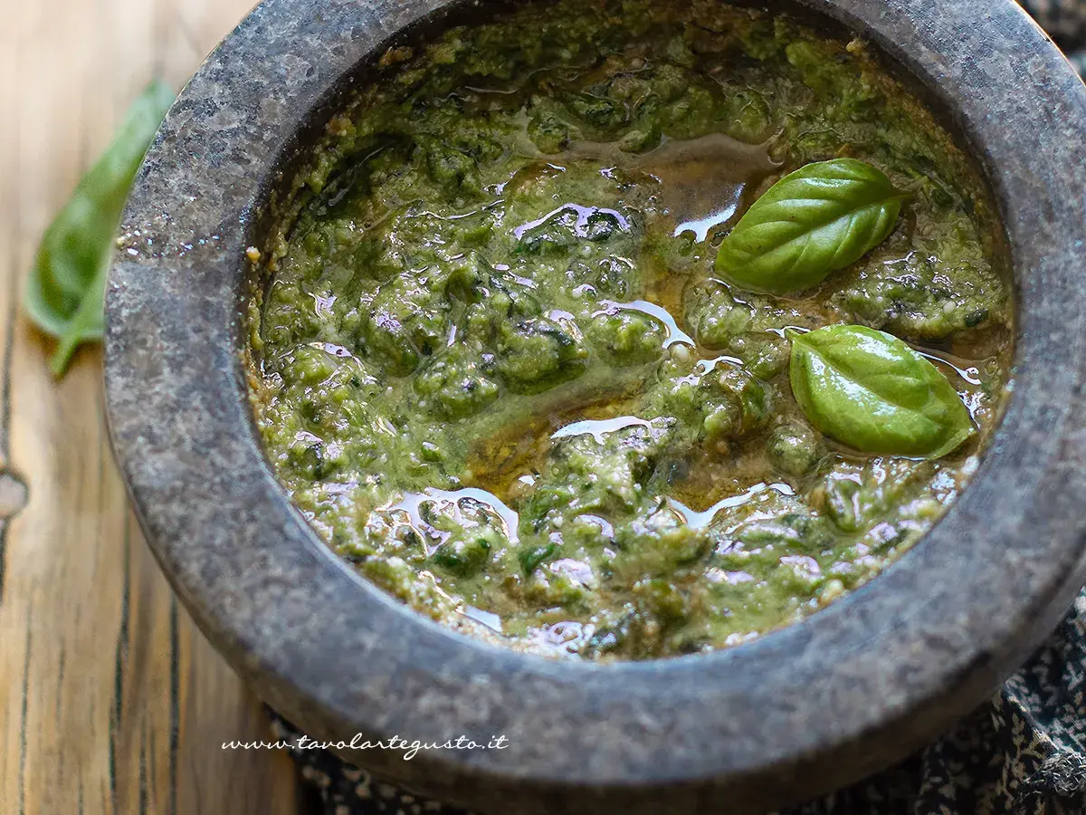Mortai con pestello pieno di profumato pesto alla genovese, guarnito con foglie di basilico fresco.