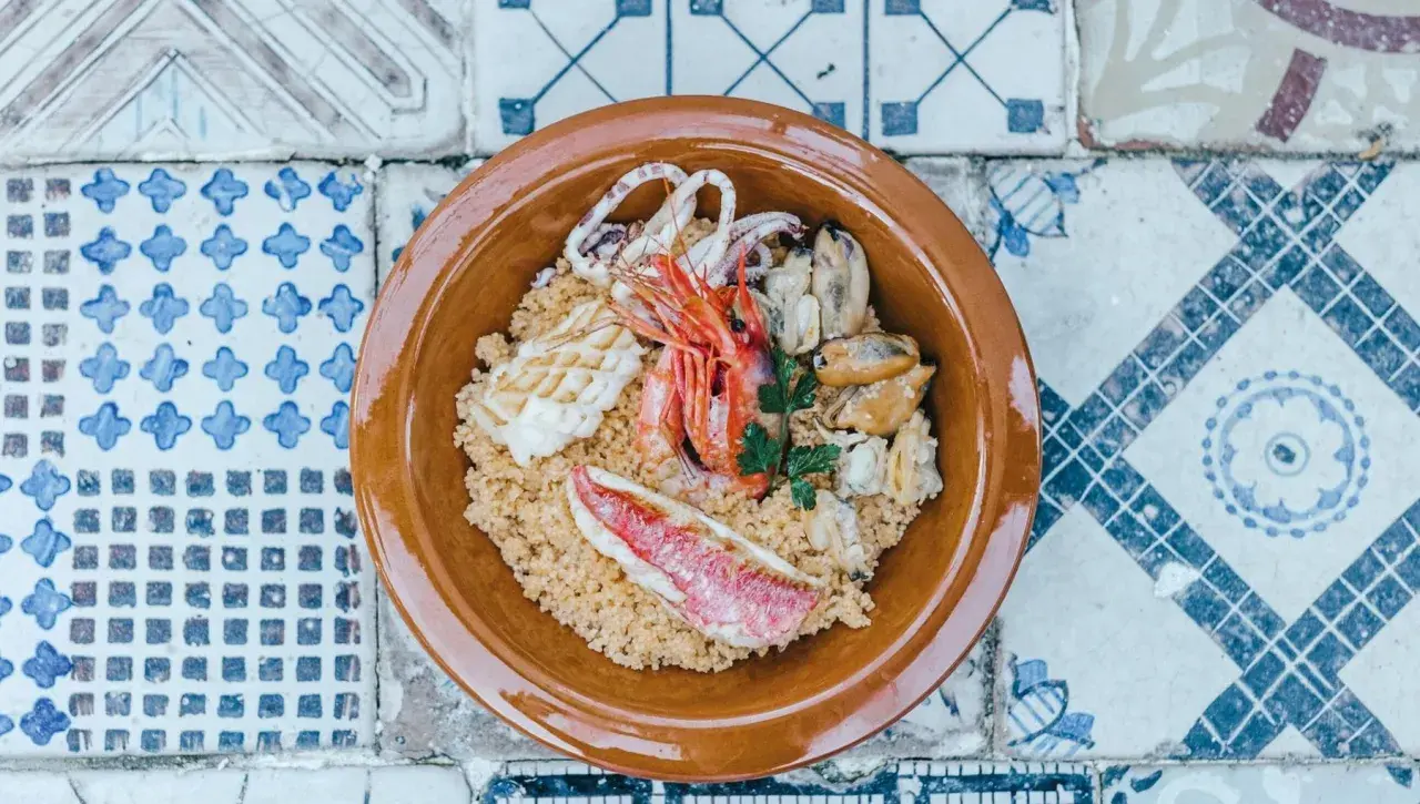 Un invitante cous cous di pesce con gamberi, calamari, cozze e pesce rosso, guarnito con prezzemolo fresco.