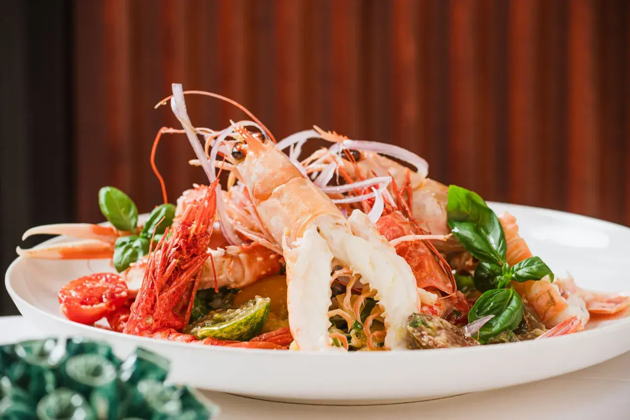 Un'appetitosa catalana di crostacei, con scampi, gamberi, pomodorini e basilico fresco, servita su un piatto bianco.