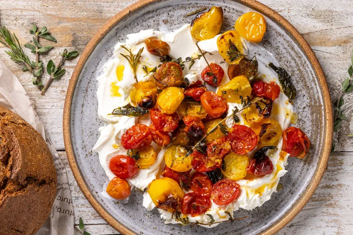 Pomodorini al forno succosi e colorati su una base cremosa, guarniti con erbe aromatiche. Perfetti con pane rustico.
