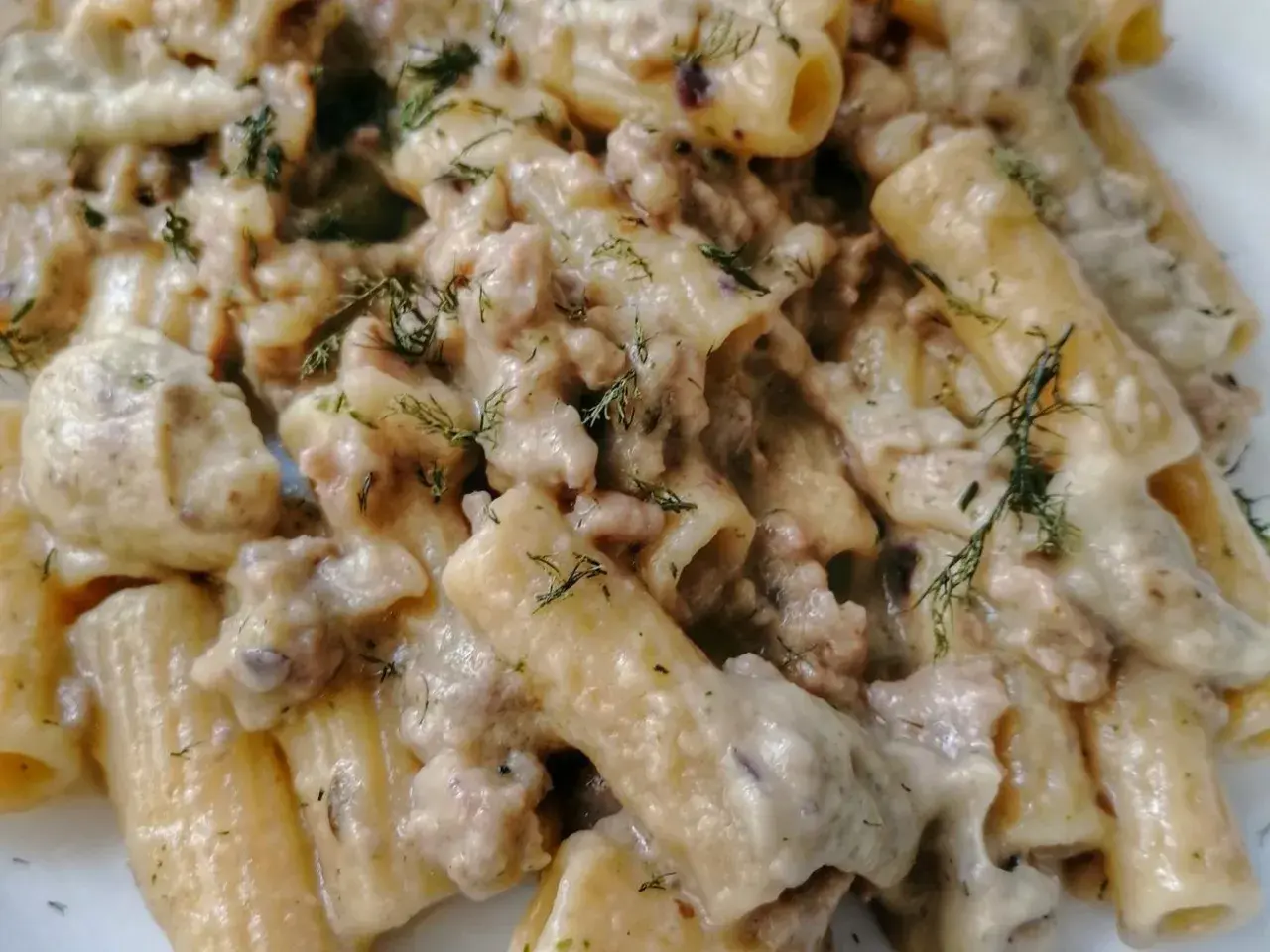 Primo piatto cremoso di pasta con tenerumi e ragù bianco, guarnito con aneto fresco.