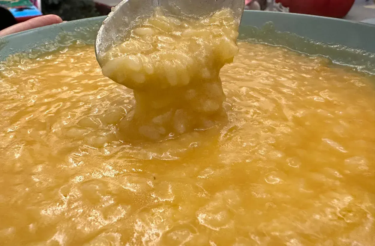 Un mestolo solleva una porzione cremosa di riso e patate, un comfort food dorato e invitante.
