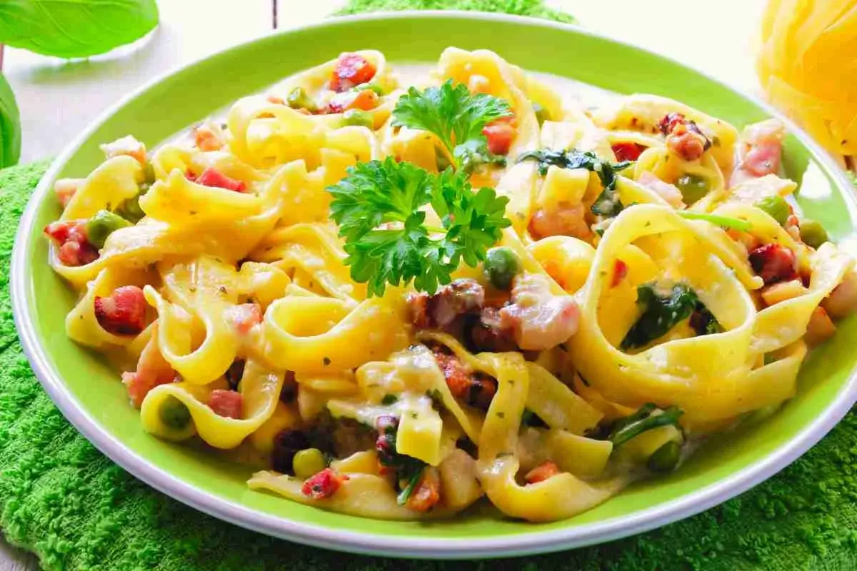 Un piatto di fettuccine cremose con piselli, pancetta e spinaci, un classico dei primi piatti pasquali.