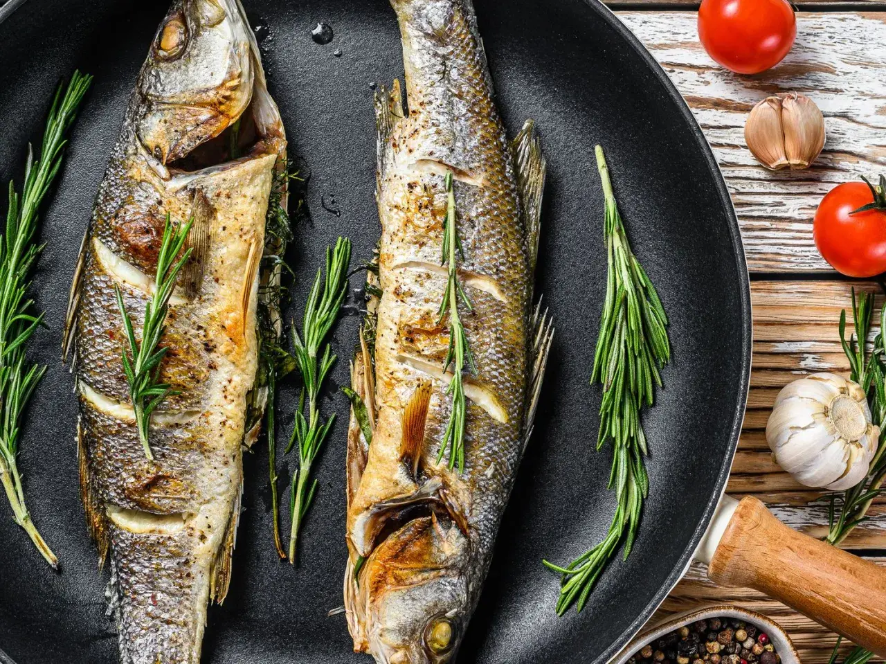 Due branzini interi cotti in padella, guarniti con rosmarino e limone. Perfetti per le tue branzino ricette.