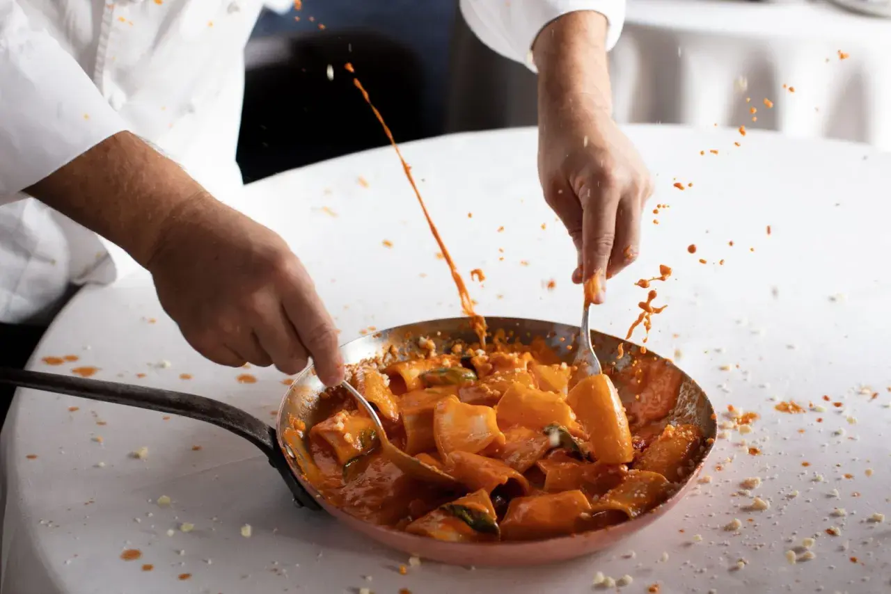 Chef mescola paccheri alla Vittorio, la salsa rossa schizza in un'esplosione di sapore.