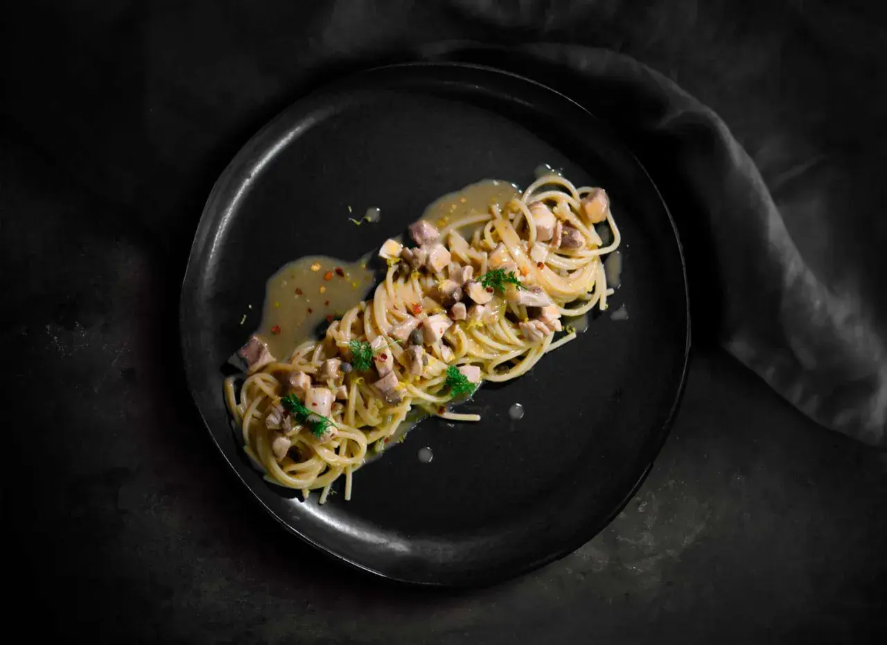 Spaghetti con ricciola, limone e peperoncino su piatto nero. Un piatto elegante e saporito.