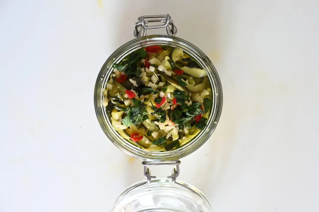 Barattolo di zucchine sott'olio con aglio, peperoncino e erbe aromatiche.