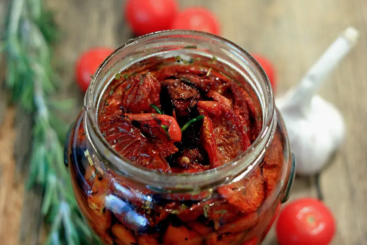 Un barattolo pieno di pomodori secchi sott'olio, un assaggio della ricetta pomodori secchi sott'olio pugliese, con aglio e rosmarino.