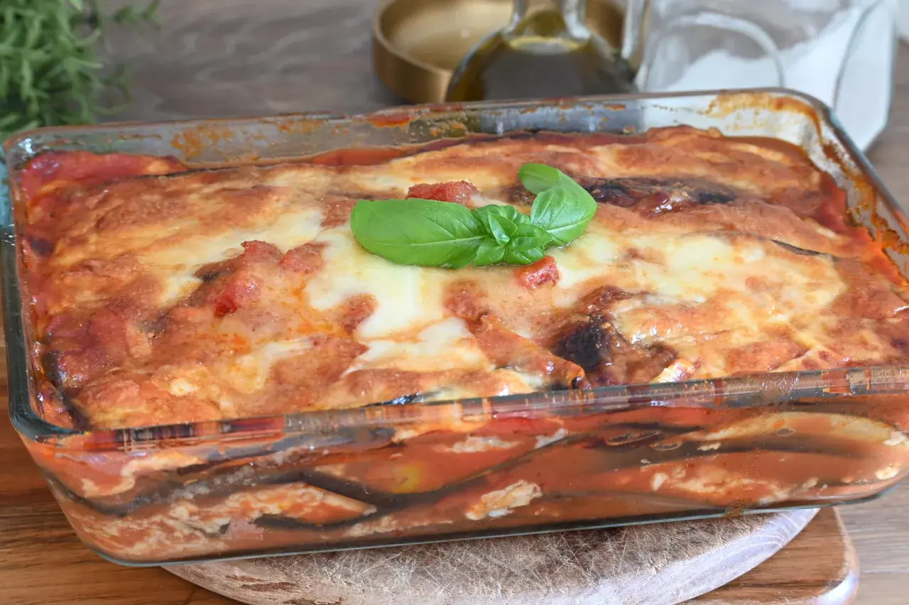 Parmigiana di melanzane non fritte, appena sfornata in teglia di vetro, con basilico fresco.