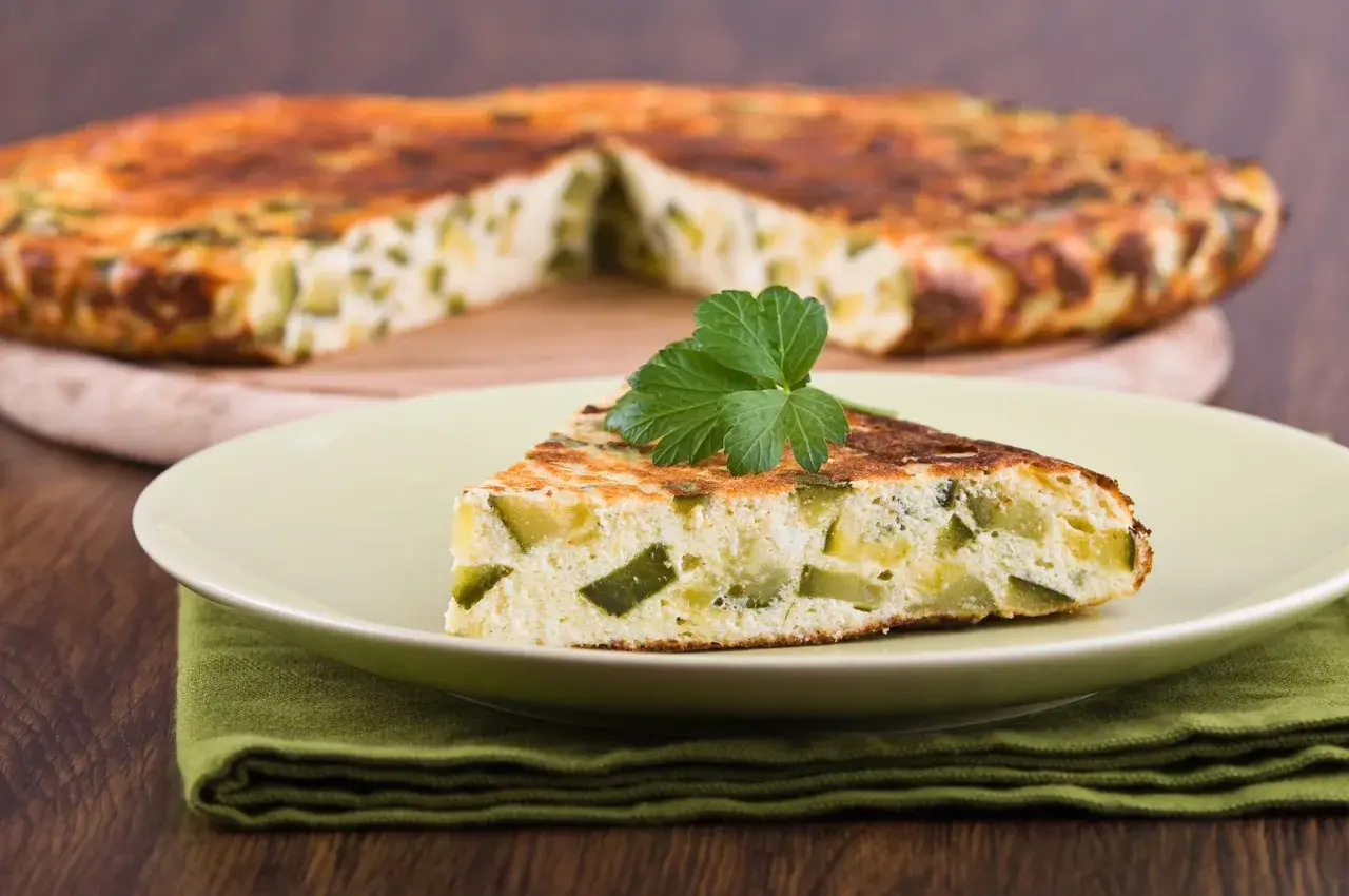 Una fetta di frittata di zucchine, soffice e dorata, guarnita con prezzemolo fresco, su un piatto chiaro.