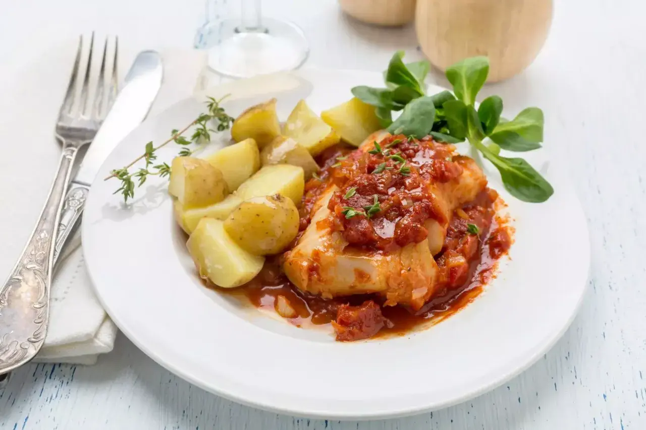 Un succulento merluzzo bollito in salsa di pomodoro, accompagnato da patate novelle e un rametto di timo.