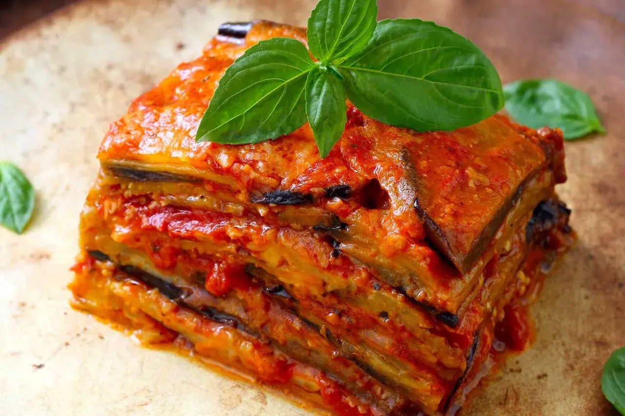 Una fetta di parmigiana di melanzane ricetta originale, stratificata e succulenta, guarnita con basilico fresco.