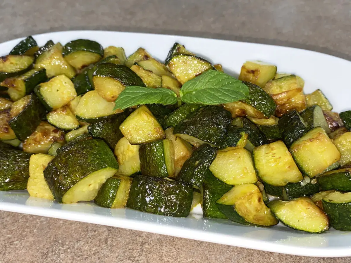 Un piatto di zucchine trifolate, tagliate a cubetti e cotte fino a doratura, guarnite con una fogliolina di menta.