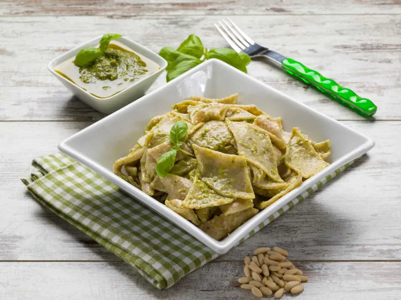 Testaroli ricetta: pasta fresca condita con pesto alla genovese, guarnita con basilico e pinoli.