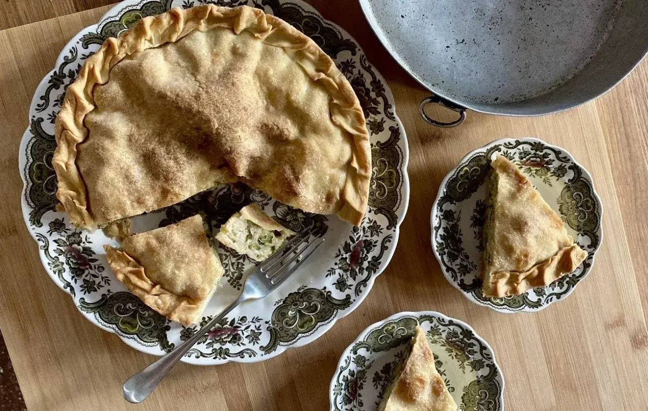 Una torta di riso e zucchine alla ligure, dorata e invitante, servita su un piatto decorato. Due fette sono già state tagliate, pronte per essere gustate.