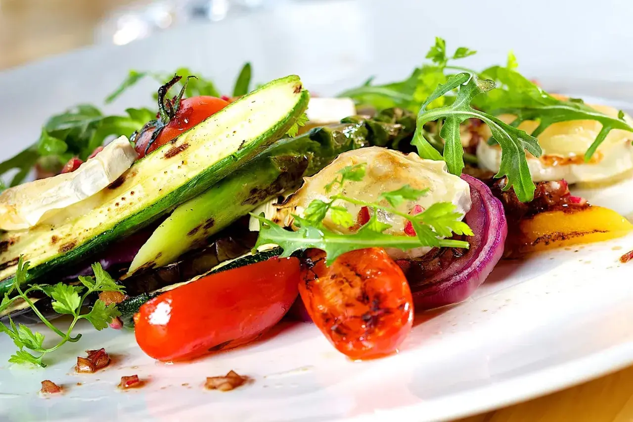 Deliziosi contorni estivi: zucchine grigliate, pomodorini, cipolla rossa e formaggio di capra su un letto di rucola.