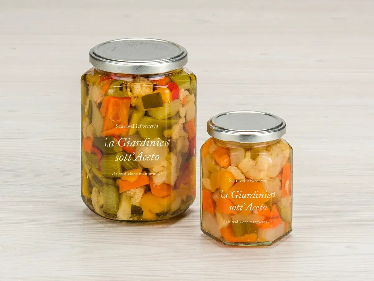 Due barattoli di giardiniera fatta in casa, pieni di verdure miste sott'aceto, su un tavolo di legno chiaro.