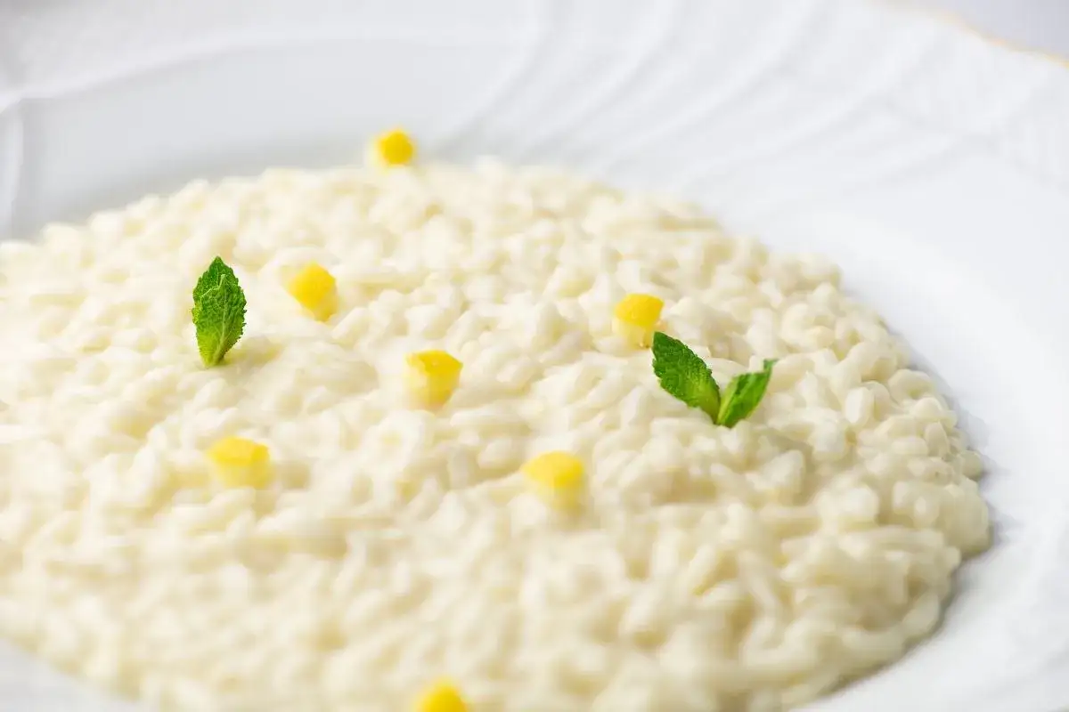 Un cremoso riso al limone, guarnito con cubetti di limone e foglie di menta fresca, servito su un piatto bianco.