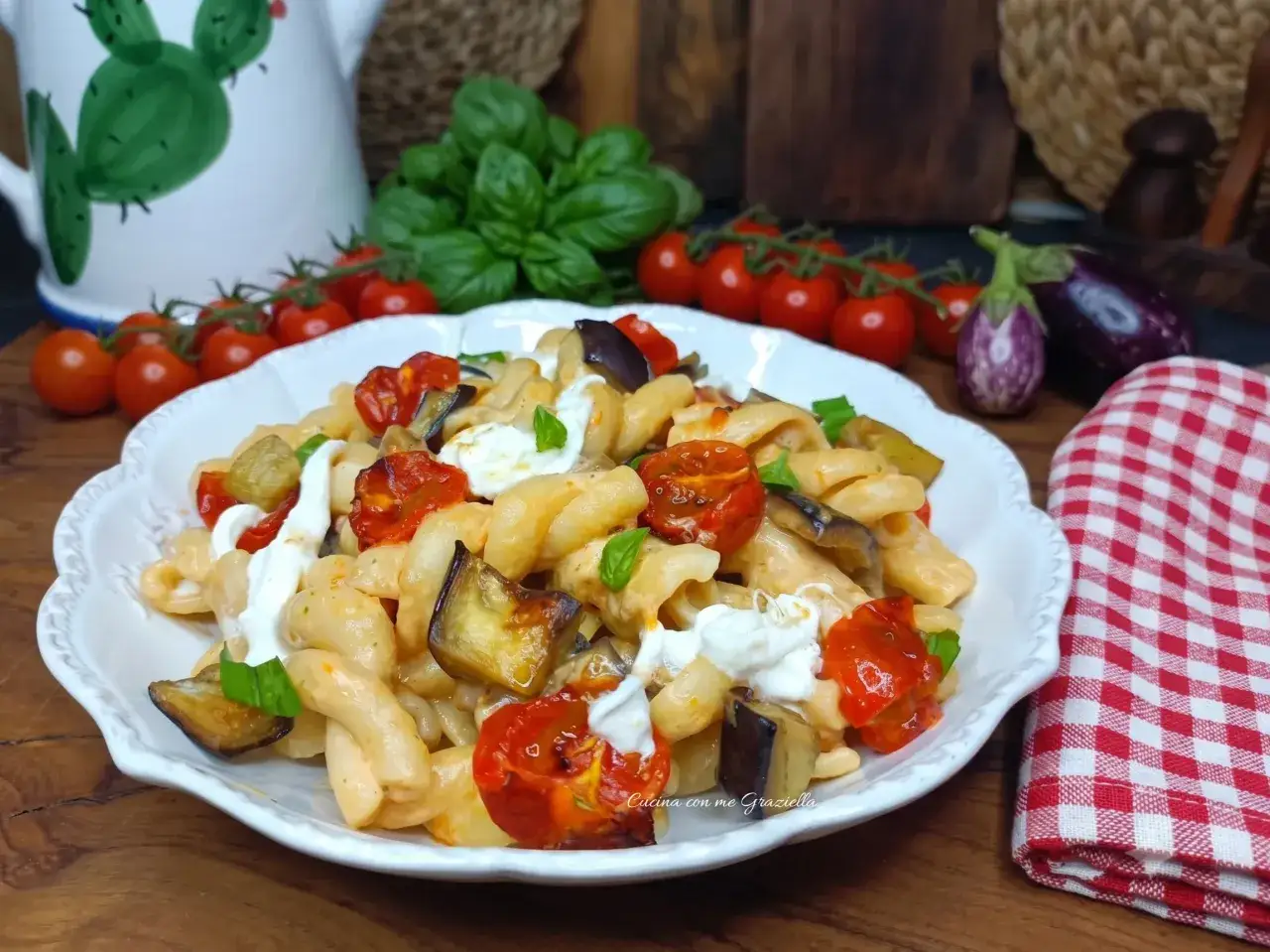Piatto invitante di pasta con melanzane e pomodorini, condita con ricotta fresca e basilico.