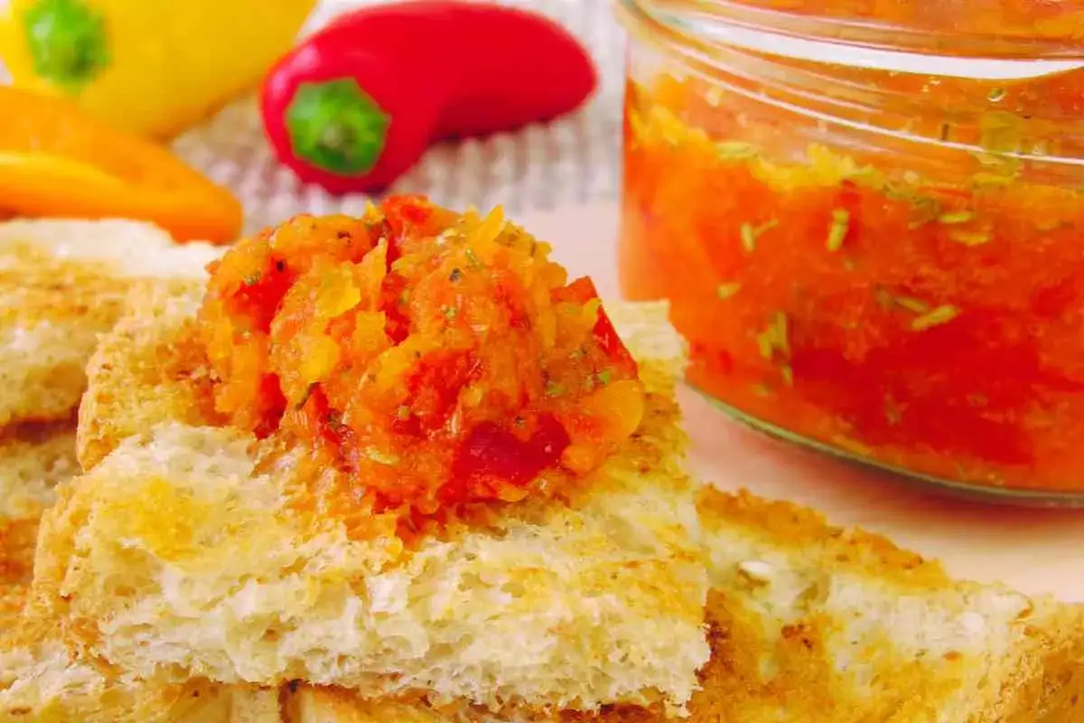Bruschette con una gustosa crema di peperoni, accompagnate da peperoni freschi e un vasetto di conserva.