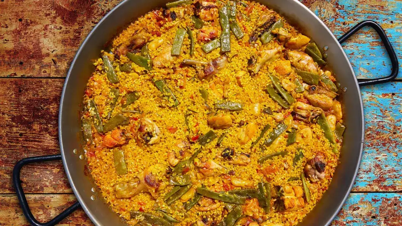 Una gustosa paella valenciana con pollo, fagiolini e riso giallo, pronta per essere gustata su un tavolo di legno rustico.