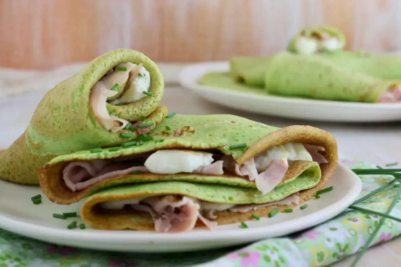Deliziose crepes di zucchine ripiene di prosciutto e formaggio, guarnite con erba cipollina. Un piatto leggero e gustoso.