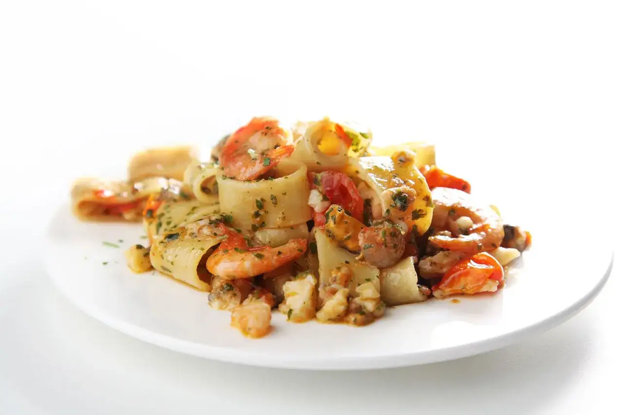 Un piatto invitante di calamarata allo scoglio, con pasta grossa, gamberi succulenti, cozze e pomodorini freschi, condito con erbe aromatiche.