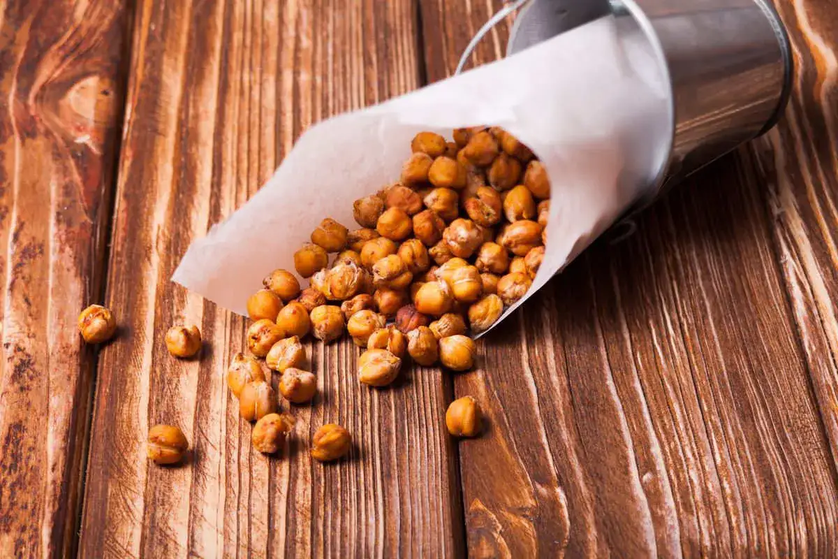 Ceci croccanti in friggitrice ad aria, versati da un cono di carta su un tavolo di legno. Uno snack salutare e gustoso.