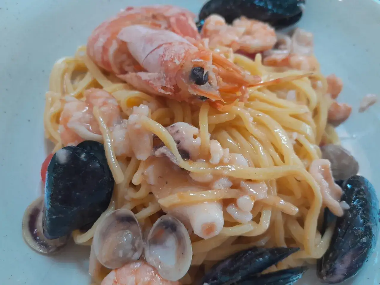 Un piatto di tagliolini ai frutti di mare con gamberi, cozze e vongole, condito con una salsa cremosa.