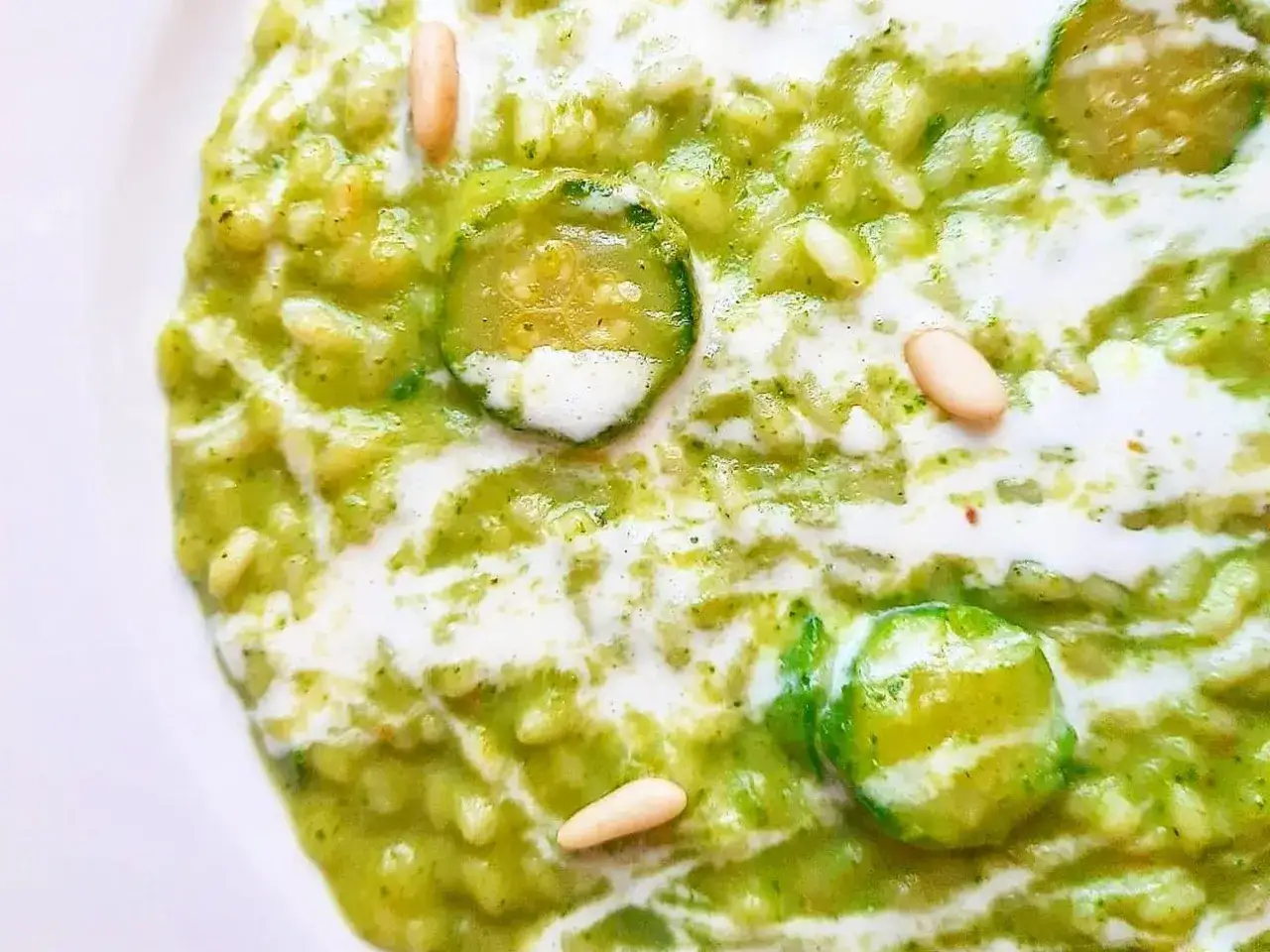 Risotto cremoso con zucchine, guarnito con pinoli tostati e un filo di panna. Un piatto fresco e saporito.