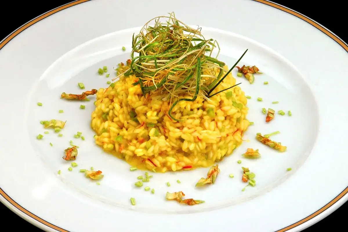 Risotto ai fiori di zucca cremoso, guarnito con erbe croccanti e petali di fiori secchi.