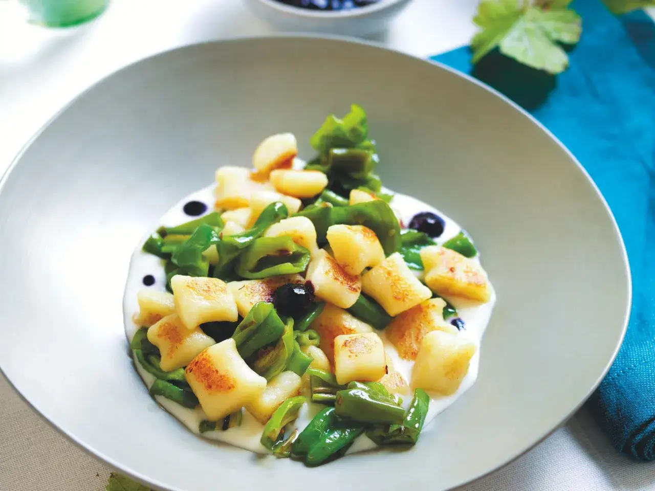 Gnocchi di patate dorati serviti con peperoni verdi, olive nere e una salsa cremosa in un piatto grigio.